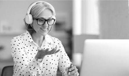 A woman wearing headphones smiles while looking at a computer screen.