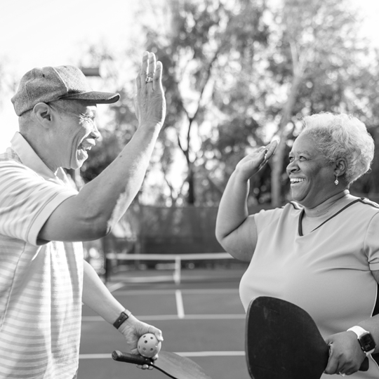 A senior man and woman give each other a high five while playing pickleball