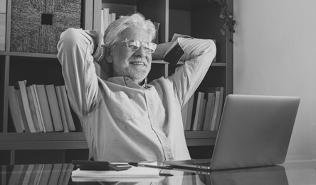A senior man smiles while looking at his laptop.