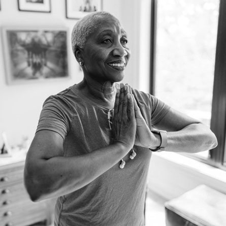 A senior woman stands in a yoga pose with hands pressed together.