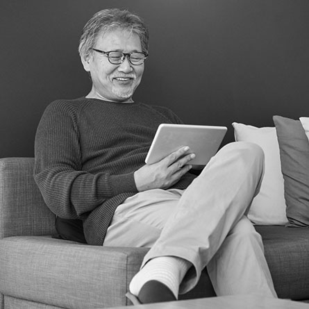 A senior man smiles while looking at his tablet.