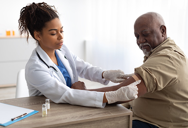 A female doctor applies an adhesive bandage to an older male patient after a vaccine.