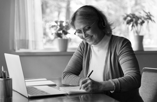 Smiling women taking notes on paper in front of a laptop