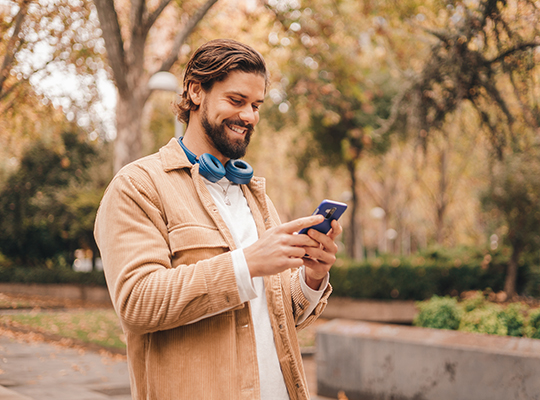 A young man standing in a park checks his health insurance benefits on his smartphone