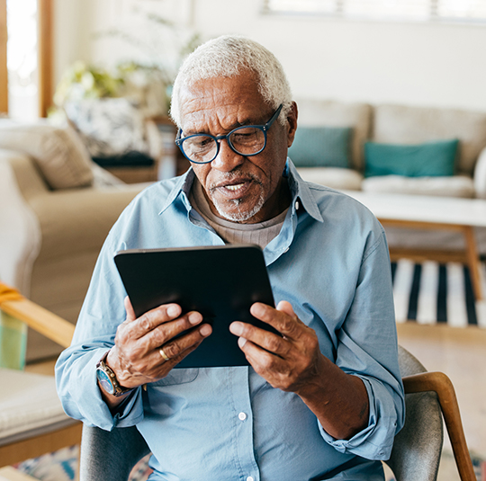 An older man looks at his tablet while sitting in his living room.