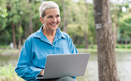 A woman smiles while sitting outside with her laptop.