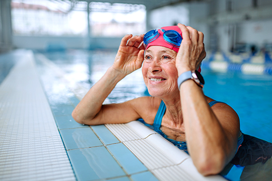 An older woman takes a break from lap swimming by lifting her goggles up.