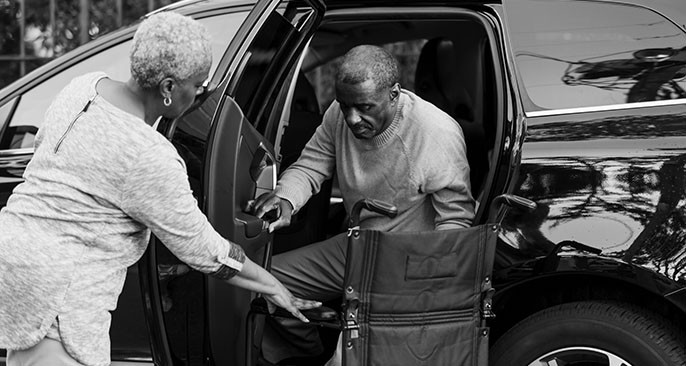 Older man being helped out of car by driver