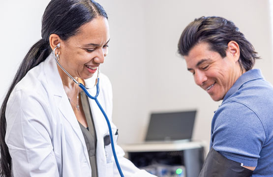 A woman in a lab coat checks a man's blood pressure with a stethoscope.