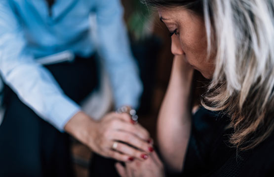 A woman holds another woman's hand during an emotional moment.