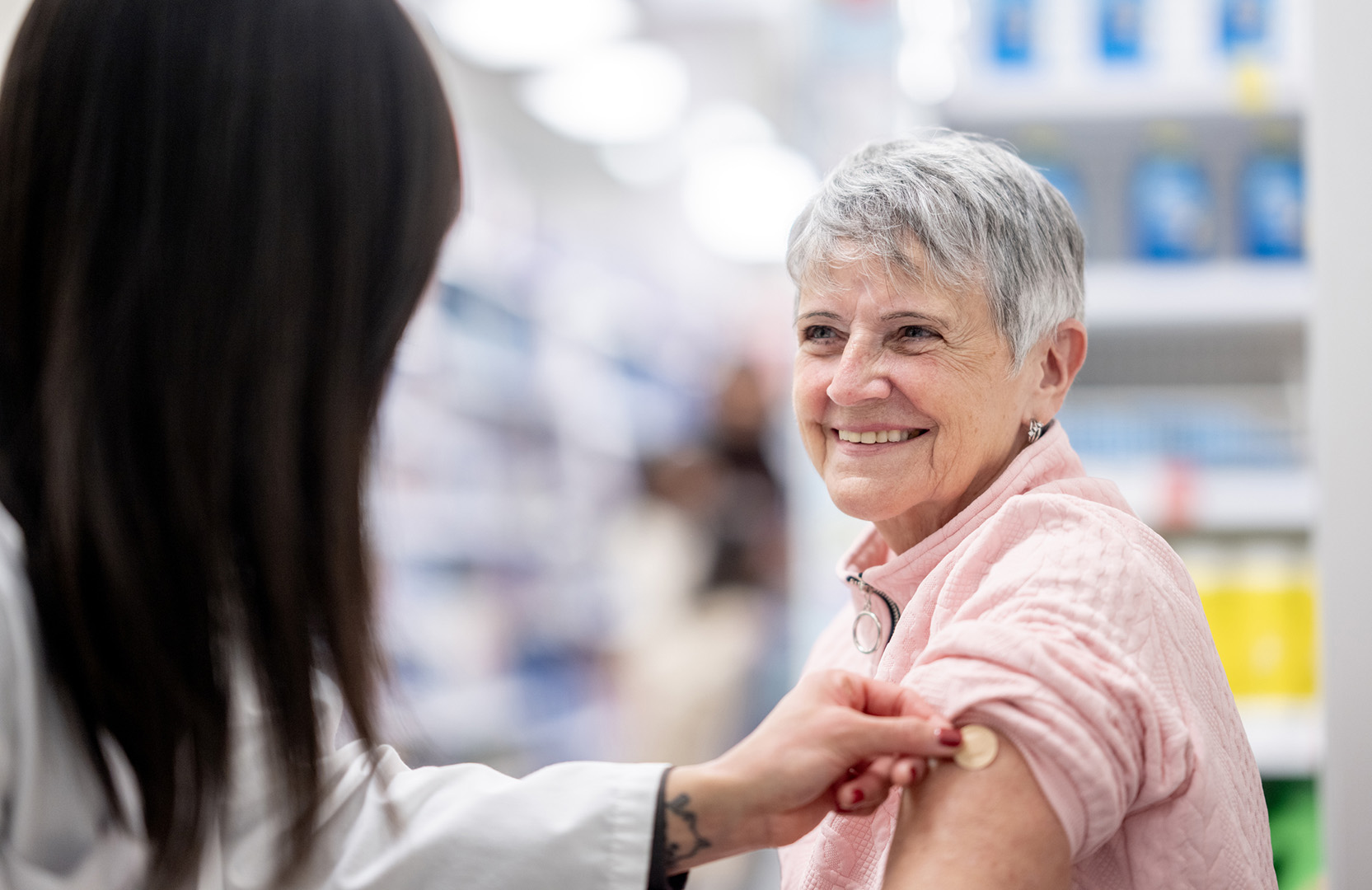 A female health care worker puts a bandage on and older woman’s arm after a vaccine.
