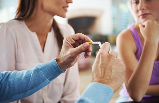 A man breaks a cigarette in front of two women.