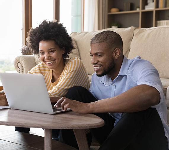 A smiling couple sits together looking at a laptop.