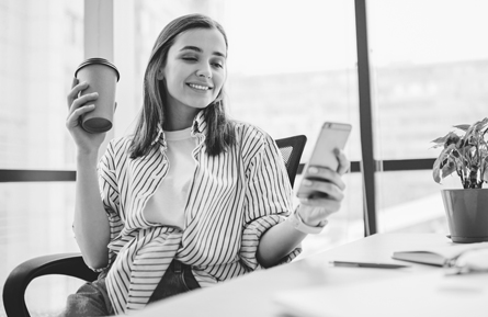 A woman looks at her mobile device while holding a cup of coffee