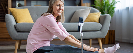 A woman doing stretching exercises on the floor while watching a webinar on her phone