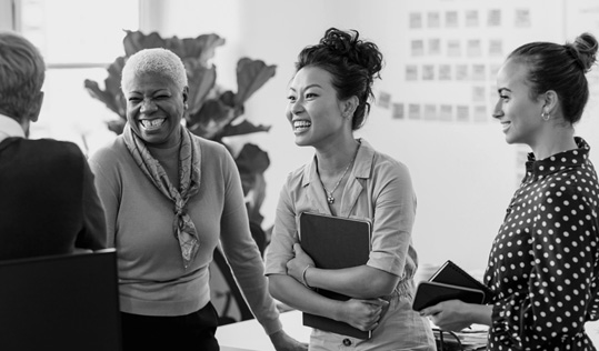 a diverse group of women stand laughing and smiling with each other