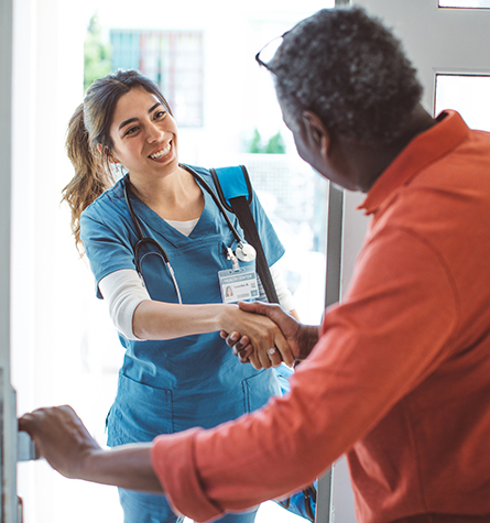 A nurse shakes hands with a patient while entering their home.