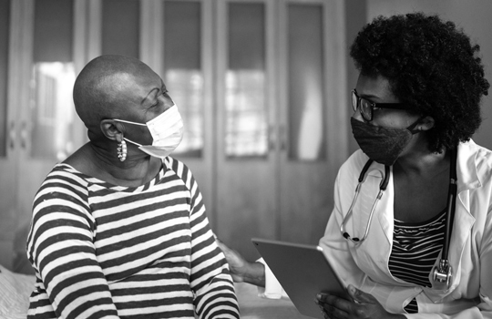 A masked doctor sits and talks with her patient. 