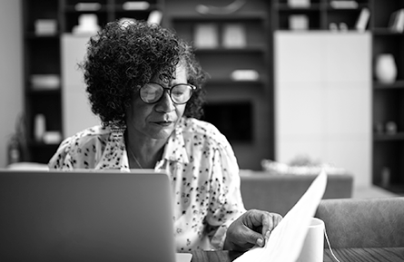 A woman sits at a desk with paperwork and a laptop