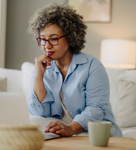 Woman wearing glasses sits on a couch using a laptop at home.