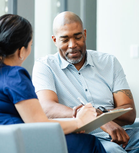 A man sits next to a healthcare provider, who is filling out paperwork.