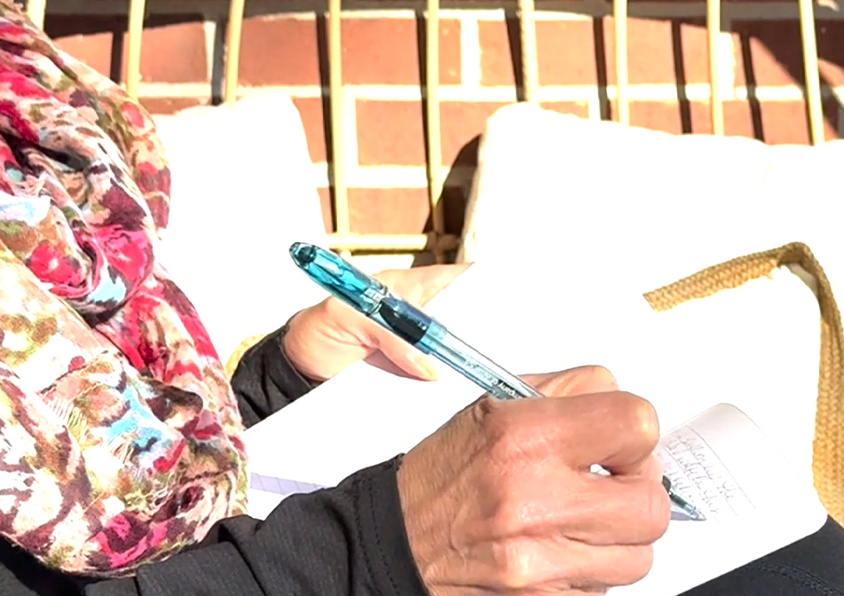 A person sits and writes on a sunny day.