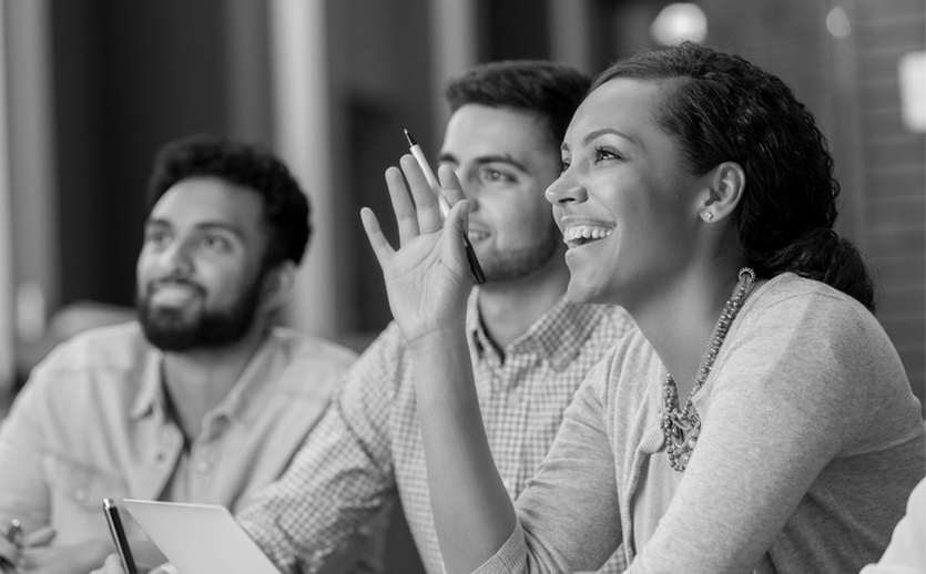 A young woman smiles, raising her hand in a meeting.