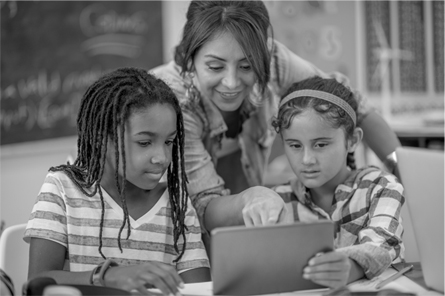 A teacher points to a tablet as two students look on