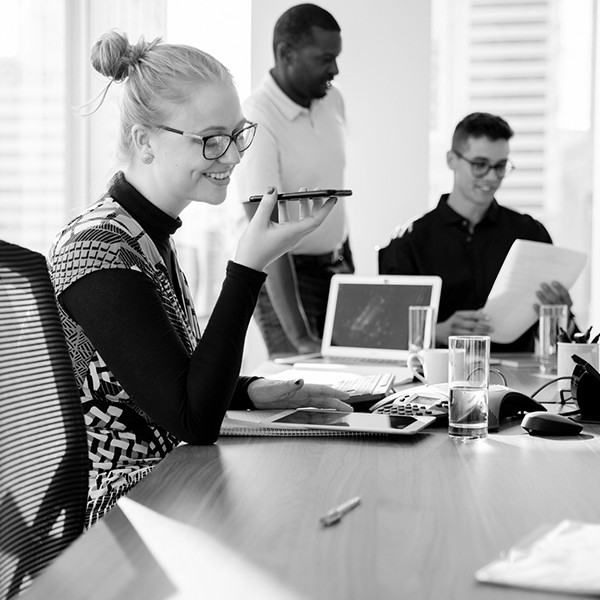 A woman talks into her phone as two people work in the background