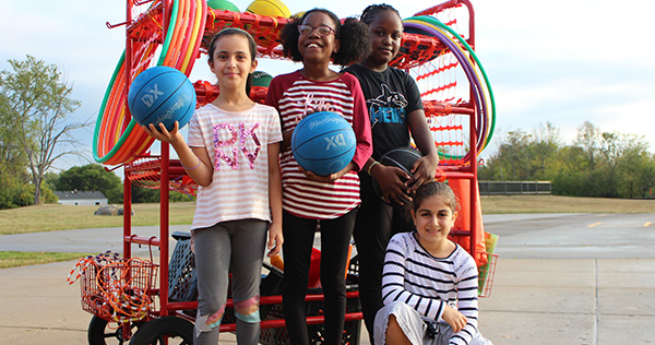 Four children pose outdoors in front of playground equipment.