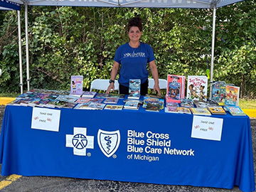 A A Blue Cross volunteer stands at a table with books and a cover showing the Blue Cross logo