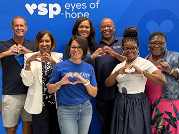 A group of adults standing together in front of a banner that says VSP eyes of hope making a heart shape with their hands