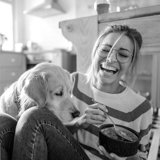 A young woman laughs as her dog begs for food