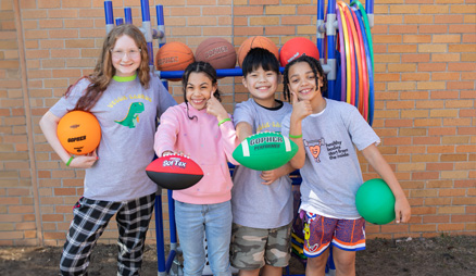 Four children hold volleyballs and footballs.