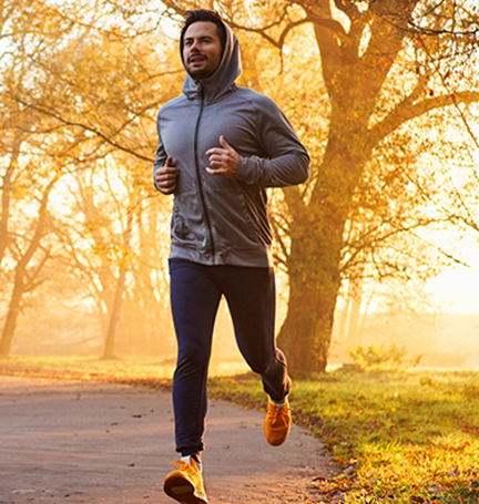 A man jogs down a path in a park at sunrise.