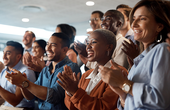 A group of diverse people stands smiling and clapping