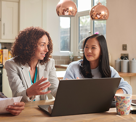 Two women sit in front of laptop and talk about work.