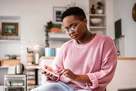 A woman sits in her kitchen using her mobile device