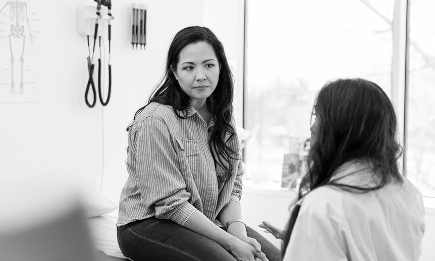 A woman sits and listens to a doctor.