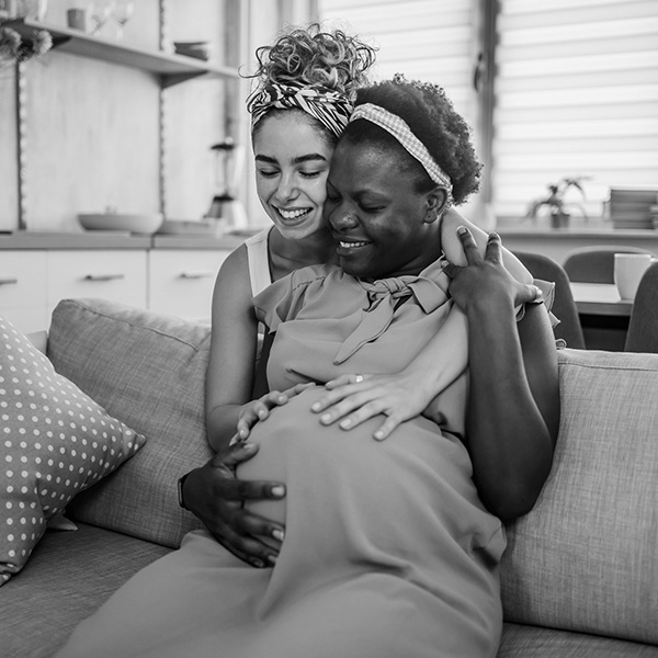 A woman feels her pregnant friend's belly.