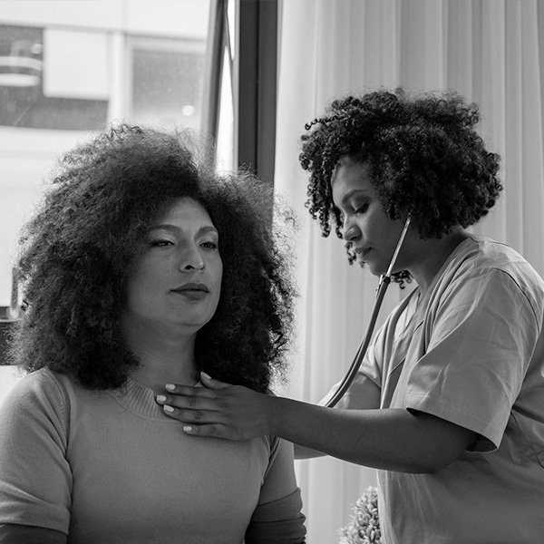 A woman sits as a doctor uses a stetoscope to listen to her heart.