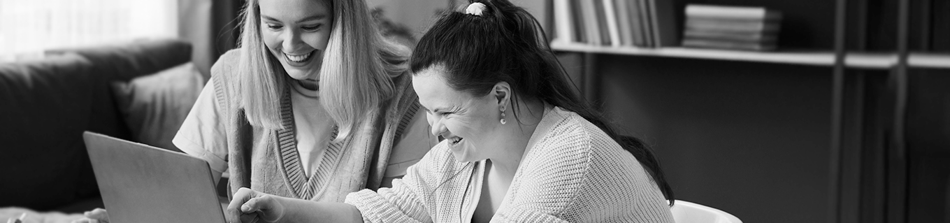 A woman helps another woman work on a laptop computer