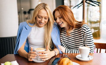 Two friends drink coffee and laugh.