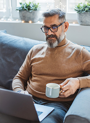 Mature man sitting on sofa at home and using laptop for Blue Cross Health and Well-Being
