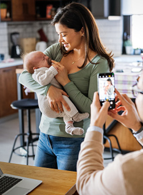 Woman holds baby as a person takes a photo with a phone