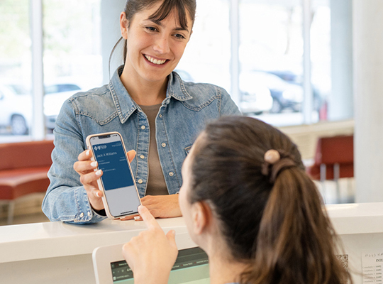  A woman showing her digital member ID to a receptionist in a doctor's office using her mobile phone