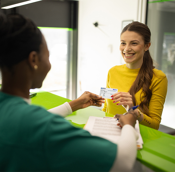 A smiling woman shows her digital ID to a receptionist