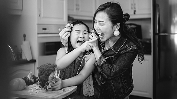 A girl and her mom play with broccoli as they cut vegetables for meal prep.