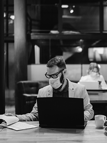 man looks at paper as he works on a laptop