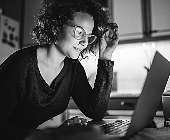 A woman wearing glasses works at her laptop